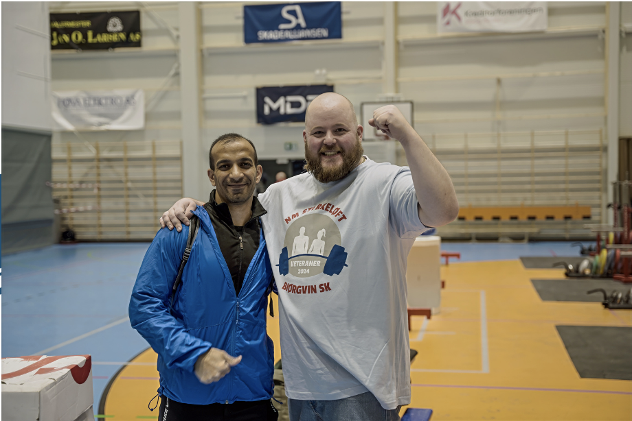 Trener følger opp en deltaker tett under styrketrening i treningssal